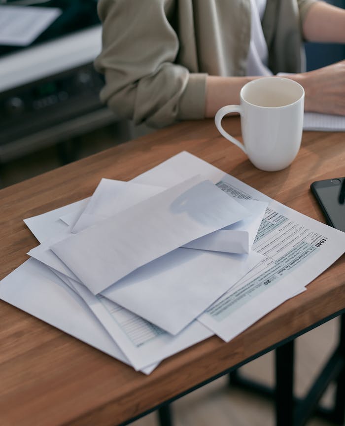 A casual workspace with envelopes, tax documents, and a coffee cup on a wooden table.